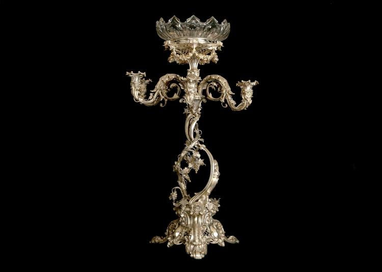 A large Victorian silver plated Rococo style table centrepiece / candelabrum, c1880. The epergne with two central twisting stems, embellished with cast leaves and berries on a tripartite base with scroll, shell and trellis work decoration, surmounted by a six branch candelabrum and stand for cut glass bowl, further decorated with wreathes, swags and acanthus leaves. The branches and top piece detachable, and the candle holders with removable sconces. Apparently no makers mark. Height (including glass bowl) 79.5cm / 31.3". Maximum width 51cm / 20". sold by Chiswick Auctions, lot 269 — auction record photograph