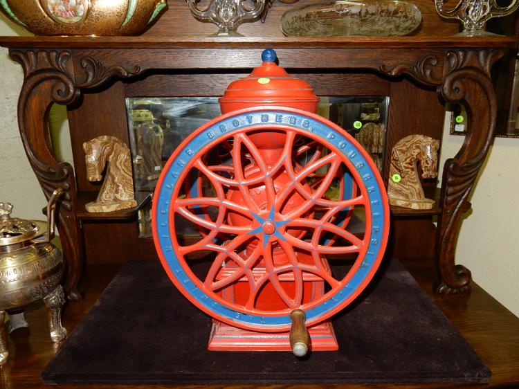Painted tabletop coffee grinder with red and blue circular wheel on a wooden table display.