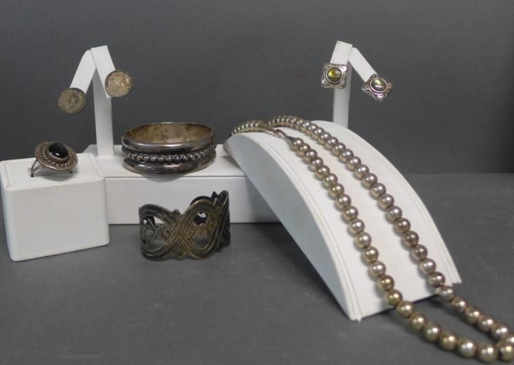 Group of silver-tone jewelry on display stands, including beaded necklaces and several rings with stone settings.