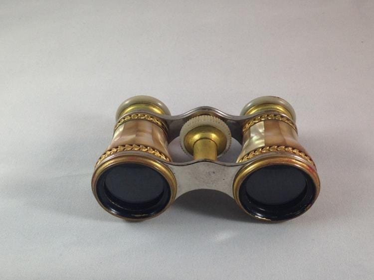 Vintage brass and silver opera glasses with dark lenses and a central focus wheel on a light background.