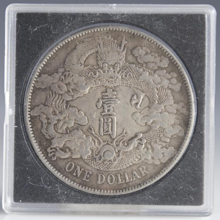 Close-up of a silver coin in a clear plastic holder, showing a dragon and cloud design with Chinese characters and the text “ONE DOLLAR.”
