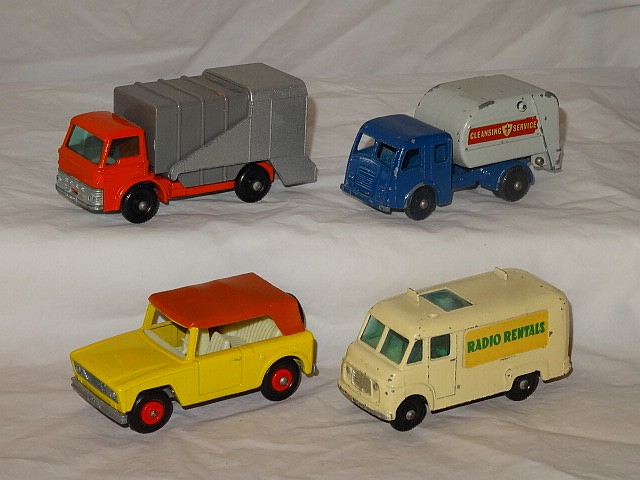 Four vintage diecast delivery trucks shown together on a white fabric background: red-gray, blue, yellow-red, and cream vans.