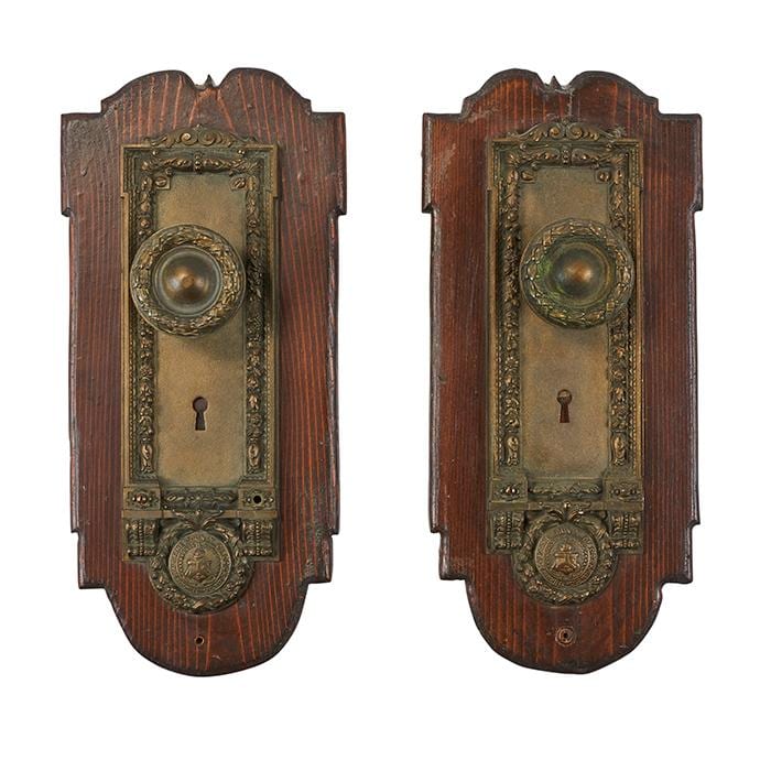 Set of two vintage door hardware escutcheons with dark brass plates, round knob surrounds, and keyhole openings on dark wood backing.