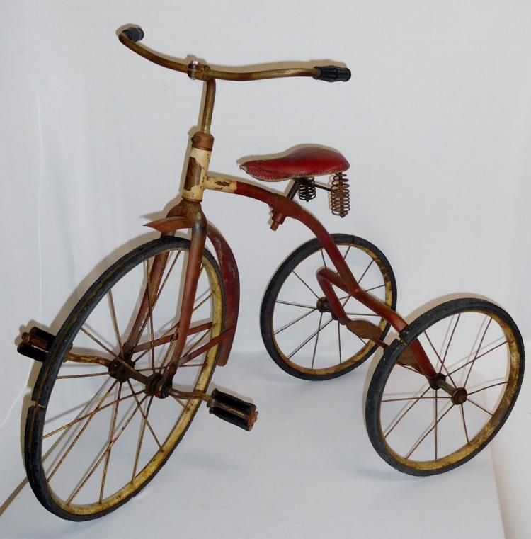 Antique child’s tricycle with a wooden frame, red seat, and two large spoked wheels, photographed against a white background.