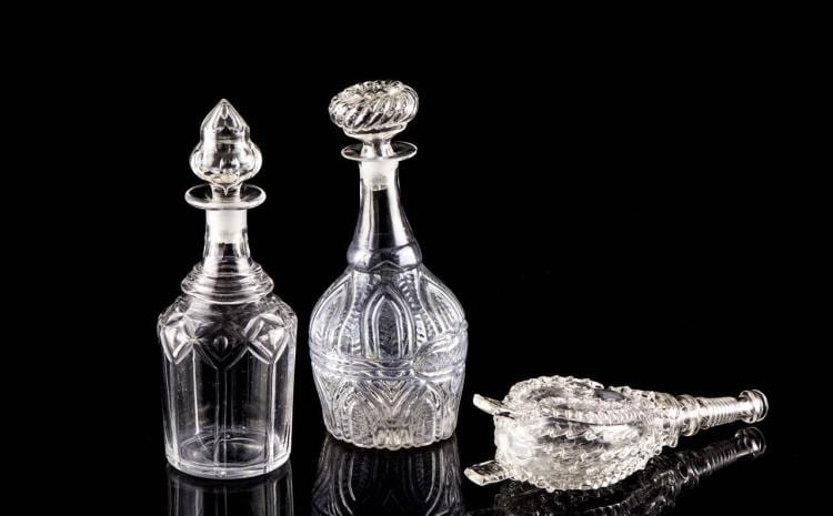 Two clear pressed-glass decanters with matching stoppers, shown beside a stopper on a black background.