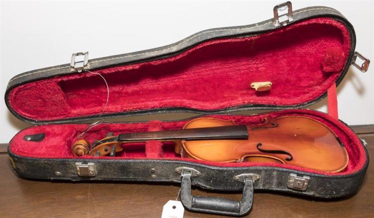 Open violin case with a wooden violin resting on bright red velvet lining, showing strings and tailpiece hardware.
