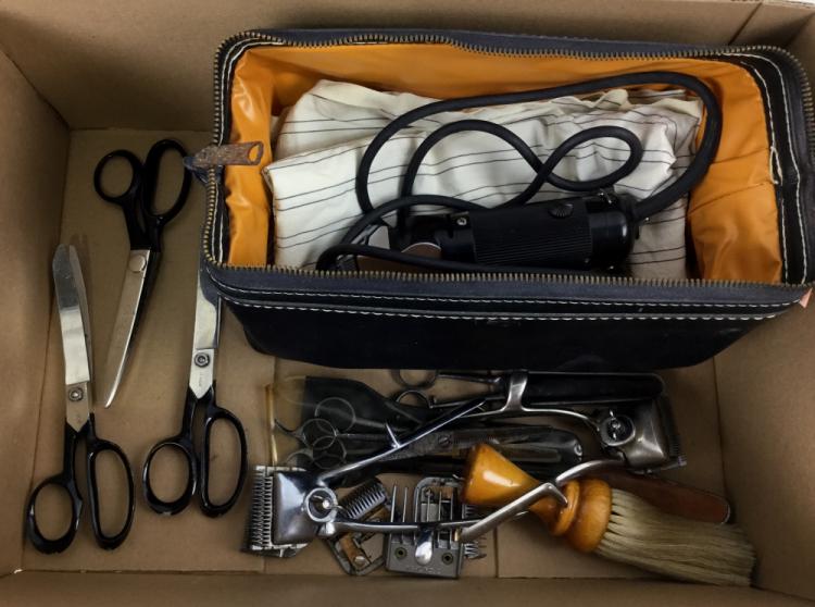 Open container holding multiple hair cutting tools including several pairs of scissors, a comb, and a brush.