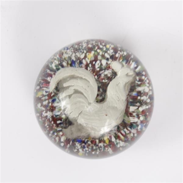 White rooster relief set into a round, multicolored speckled glass paperweight on a light background.