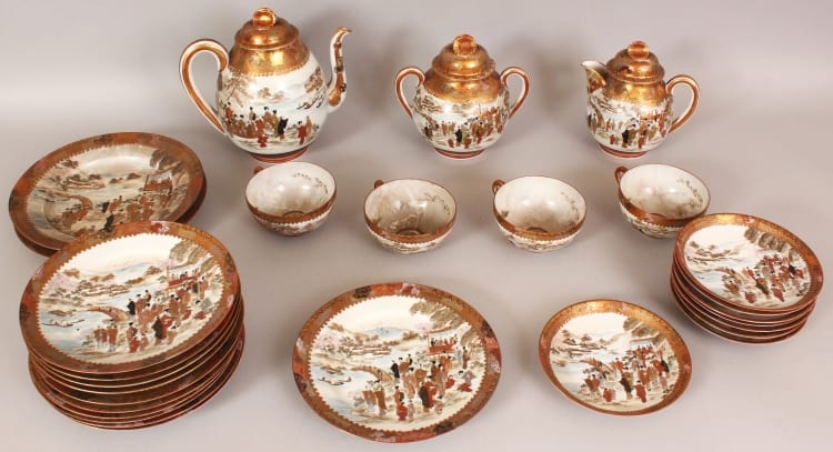 Japanese Kutani-style porcelain tea service pieces with brown and red landscape figures on round saucers and bowls, and three covered teapots and handles.