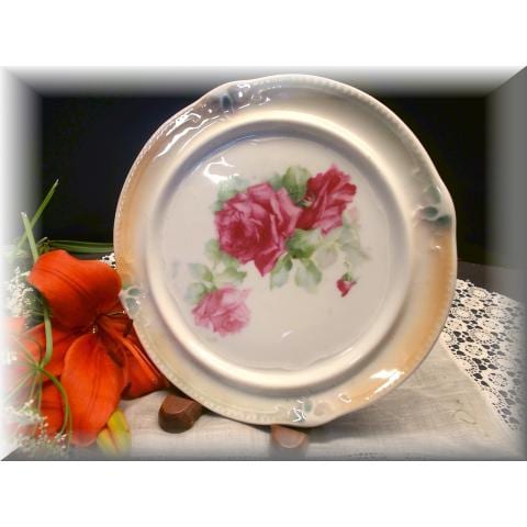 Round ceramic trivet or plate with scalloped edge, painted with pink roses in the center, on a lace cloth.