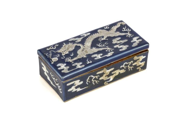 A CHINESE POWDER BLUE AND WHITE SLIP DECORATED ‘DRAGON’ BOX. Qing Dynasty. Decorated with a dragon chasing a flaming pearl among clouds and flames, made out in incised details, 7 x 19.5 x 9.5cm, together with a famille verte jar and cover, a pottery figure and a qingbai glazed jar. (4) 清   灑藍地龍盒 sold by Chiswick Auctions, lot 388 — auction record photograph