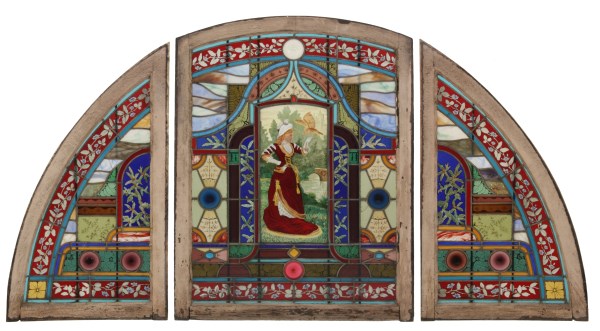 Leaded stained glass transom window panel with arched frame, red-robed figure centered, blue and red geometric and floral border patterns.