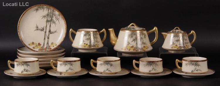 Japanese-style Kutani tea set with a decorative plate, teapot and creamer covered with gold trim, and matching cups on a dark background.