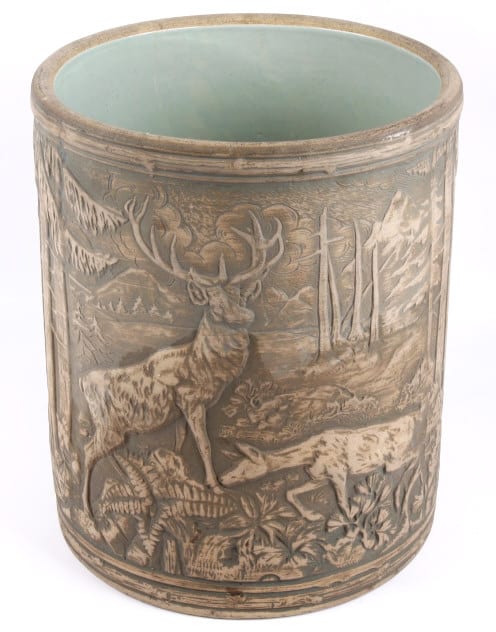 Brown stoneware crock with embossed wildlife scenes, including a stag, fish, and plants, and a light blue-green interior rim.