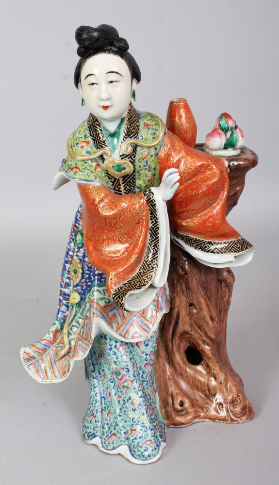 A GOOD QUALITY EARLY/MID 20TH CENTURY CHINESE FAMILLE ROSE PORCELAIN FIGURE OF A ROBED LADY, leaning against a tree stump bearing a plate of peaches and a vase, 11in high. sold by John Nicholson's Fine Art Auctioneers & Valuers, lot 542 — auction record photograph