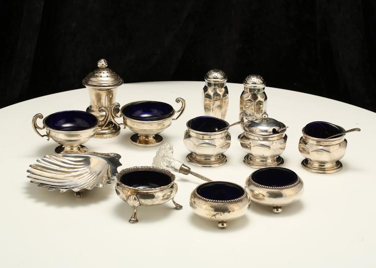 A mixed group of antique sterling silver condiment items Comprising: a George V five-piece condiment set, Birmingham 1916 and 17, by Atkin Brothers, including two pepper casters, two salts and a mustard pot, with panelled sides, the pots with blue glass liner, height of peppers 7.5 cm/2.9 inches, a pair of George V salt cellars, Birmingham 1911, by William Hutton and sons, of circular form with flying scroll handles, with blue glass lines, a pair of cauldron salt cellars, stamped sterling, probably American, a Victorian shell butter dish, London 1891, by Charles Boyton II, a cauldron salt cellar, Chester 1897, with blue glass liner, an unmarked pepper caster, a condiment spoon with glass handle, two salt spoons and an electroplated example. (Qty). Weight of silver – 598 grams/19.2 ozt sold by Chiswick Auctions, lot 87 — auction record photograph