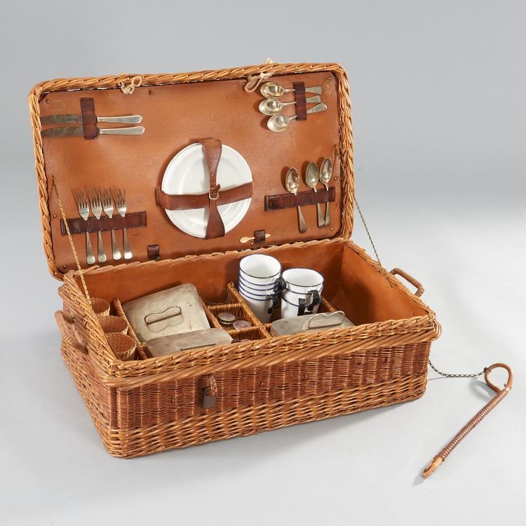 Wicker picnic basket open to show a leather-lined interior with utensils, plates, and small tableware compartments.