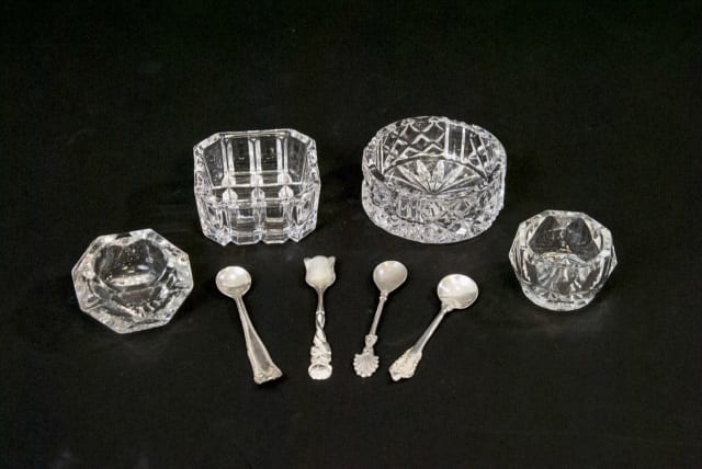 Set of crystal salt cellar pieces with small metal scoops and lids on a dark background, including several cut-glass containers.