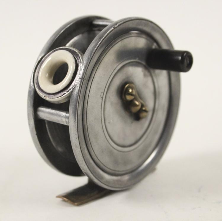 Vintage fly fishing reel with a metal spool and side handle, shown in close-up against a light background.