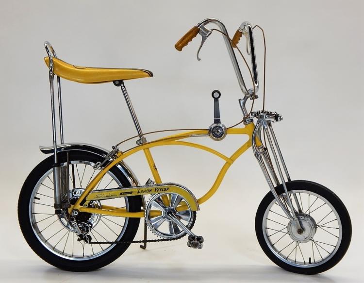Yellow Schwinn-style small bicycle (children’s bike) with chrome frame and front headlight on a studio background.