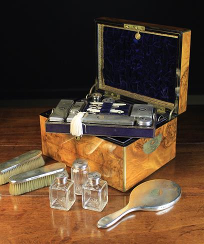 A Superb Quality Victorian Burr Walnut Vanity Box with Silver Fittings hallmarked London 1857 and stamped with Thomas Johnson I's maker's punch. The rectangular box having brass trimmed edging, an elaborate scrolling plaque to the hinged lid inscribed ''ES Bibby'' and inset brass swing handles either side embellished with engraving. The interior housing a variety of fine cut glass silver-topped bottles and jars; fitted in partitioned trays lifting out to reveal a silver backed brush & mirror set below. The silver ware all intricately machine engraved and monogramed ESB. The interior lined in deep ultramarine blue velvet with tooled gilt leather borders; the lock engraved PATENT S. MORDAN & Co LONDON. The locking base drawer fitted with padded jewellery compartments. 7½ in (19 cm) high, 13 in (33 cm) wide, 9¾ in (25 cm) deep. sold by Wilkinson's Auctioneers, lot 10 — auction record photograph