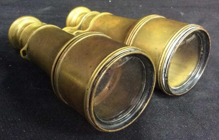 Two gold-toned opera glasses lying on a dark surface, showing their circular viewing lenses and cylindrical bodies.