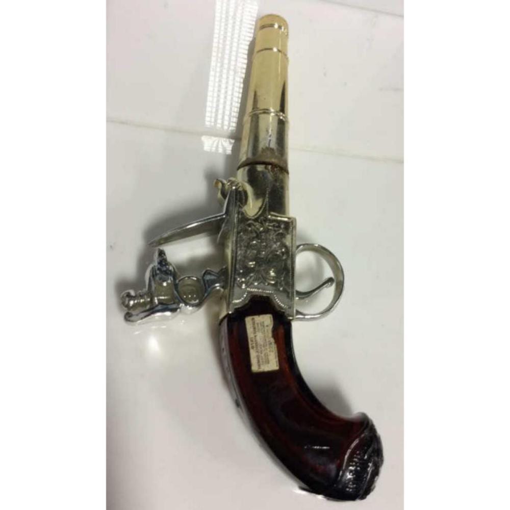 Gold and silver novelty perfume bottle shaped like a handgun with a handgun-shaped cap and amber liquid inside.