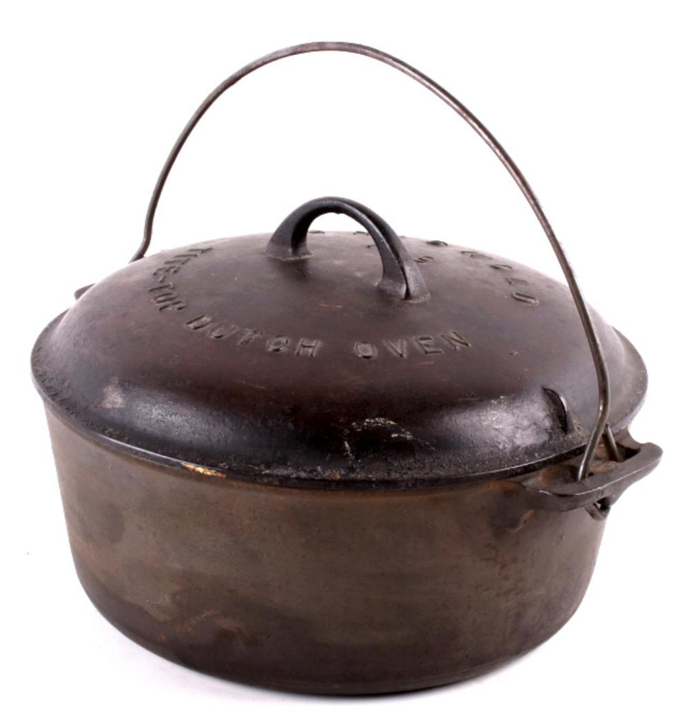 Cast iron dutch oven with a domed lid, loop handle on the lid, and side latch clips; brown-black metal with wear.