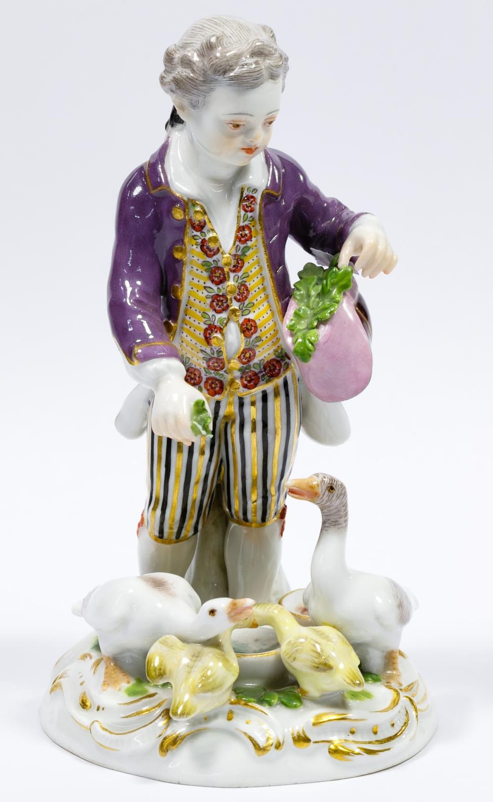 Porcelain figurine of a dressed man holding a basket or cloth with green grapes, standing over a base with white birds or ducks.
