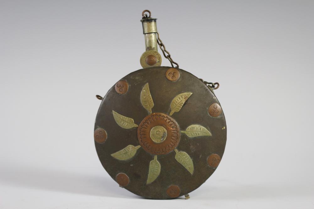 Round metal powder flask with an ornate floral medallion design on the front and a hinged cap attached by a chain.