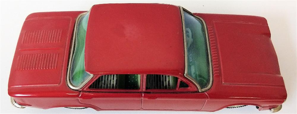 Red tin toy sedan car with a green windshield and dark window openings, photographed from above.