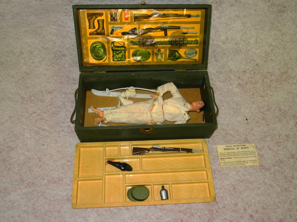 Vintage-style toy action figure in white uniform lying inside a green wooden-style foot locker case with accessory tray and printed accessory background.