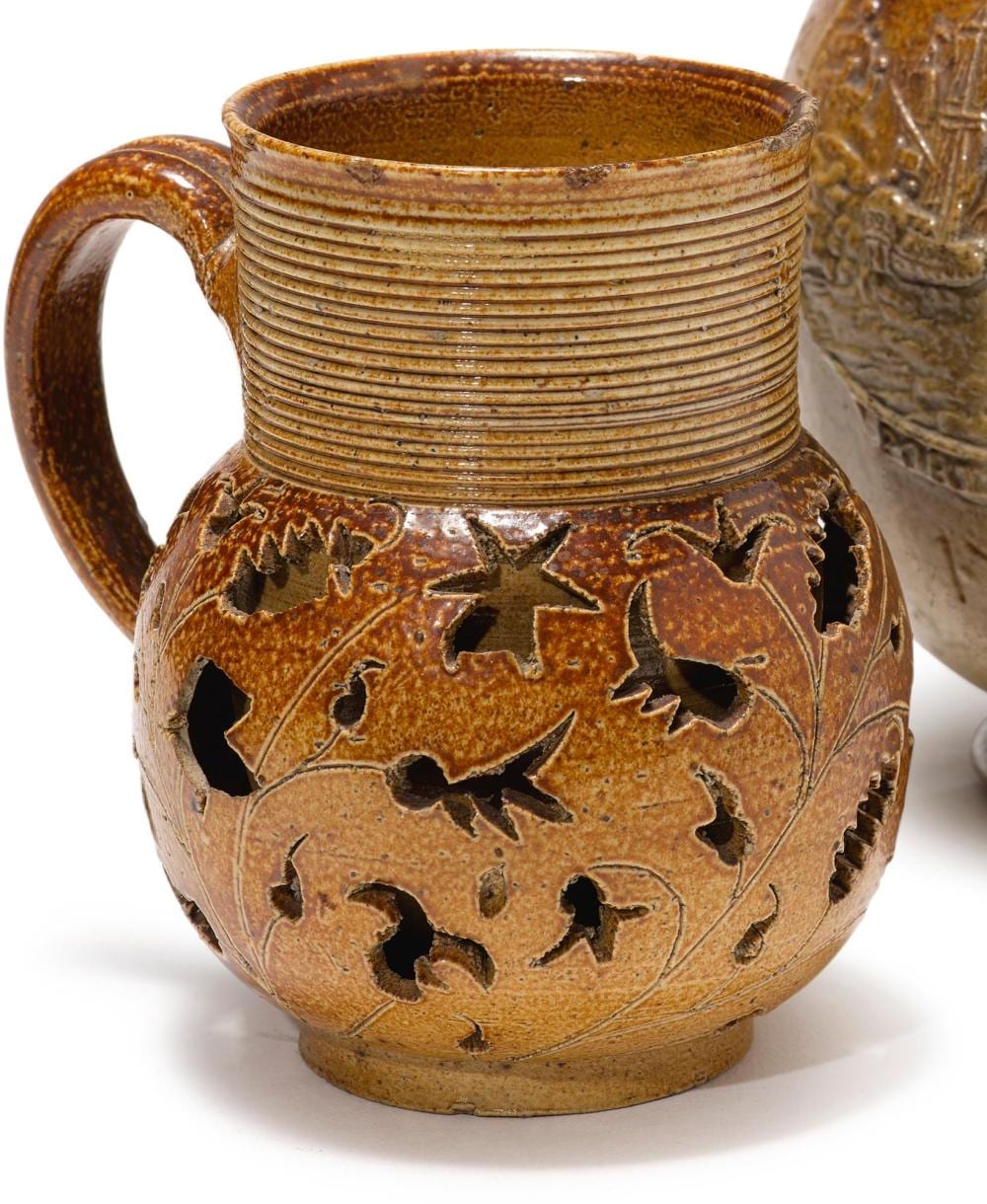 Brown salt-glazed stoneware jug with a loop handle, fluted neck, and carved floral decoration on the body.