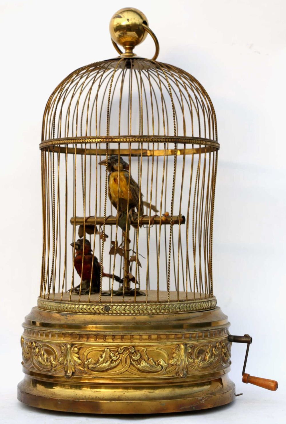 Brass-gold birdcage automaton with a round top and hanging bars, containing small painted birds inside and a crank on the base.