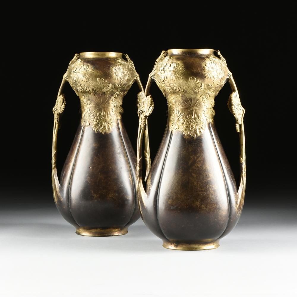 Photograph of a pair of decorative Art Nouveau style metal vases with gilt rims and floral embossed designs, shown side by side against a dark background.