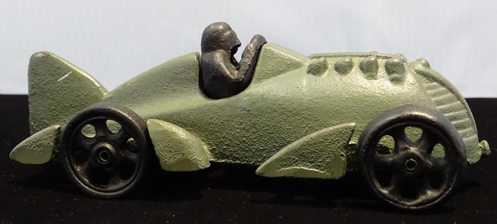 Green and black cast metal boat-shaped toy racer with open wheels and a small horn-like figure on top.
