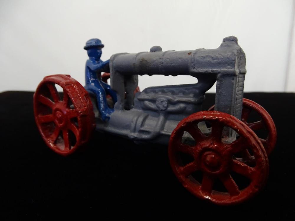 Small cast metal farm tractor toy with a blue body and red spoked wheels, viewed in three-quarter angle.