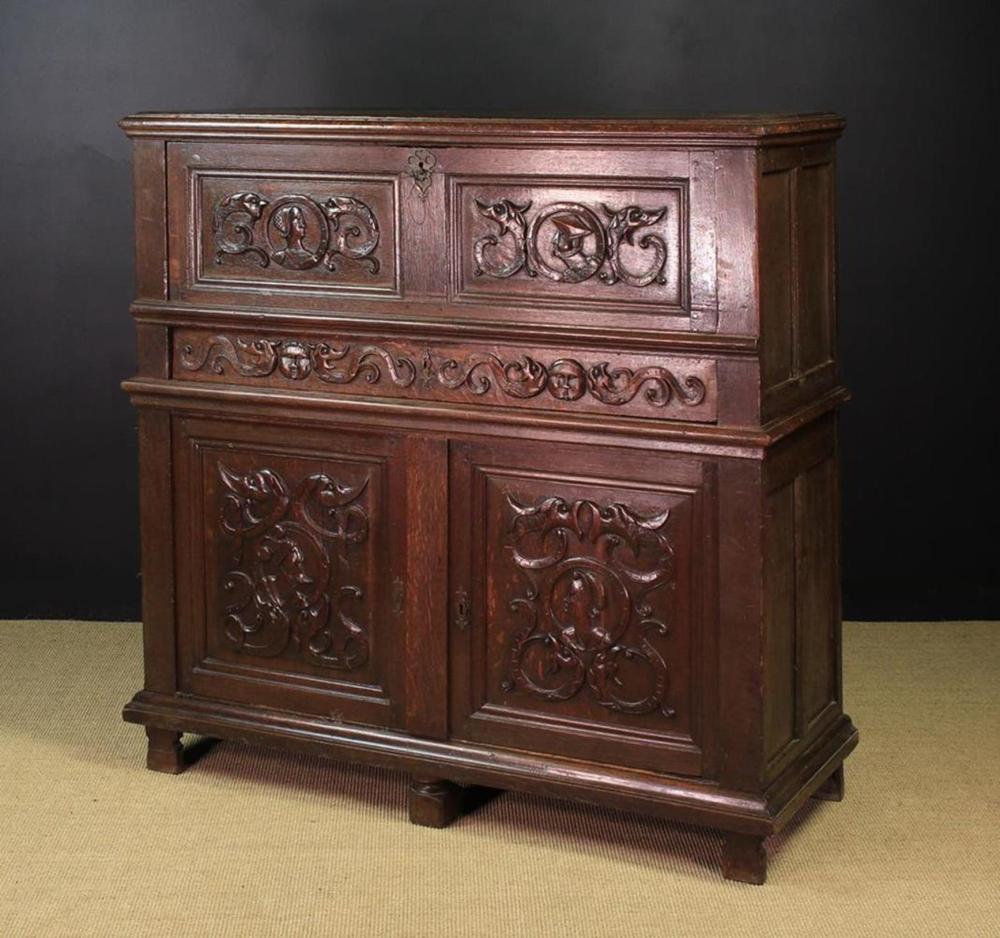 A 16th Century Carved Oak Secrètaire Cabinet in two sections. The upper section having a fall front compartment with a twin panelled facade enriched with Romayne portraits flanked by zoomorphic scrolls of foliage above a long frieze drawer with sold by Wilkinson's Auctioneers, lot 582 — auction record photograph