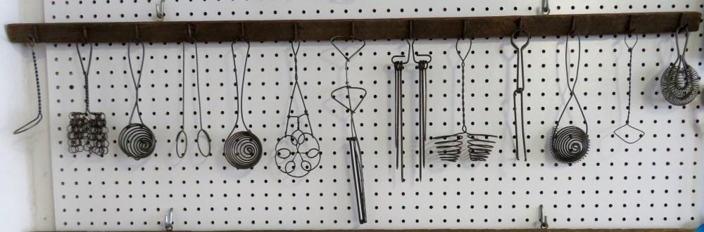 Row of hanging metal kitchen utensils and tools on a pegboard display, including strainers and ladle shapes.