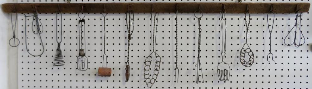 Row of vintage kitchen utensils hanging on a pegboard, including ladles, whisks, and strainers.