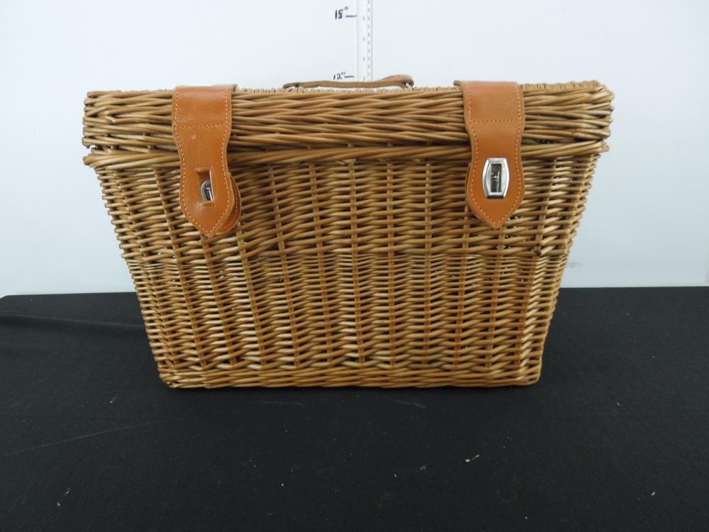 Woven wicker picnic basket with tan leather straps and buckles, photographed against a light background.