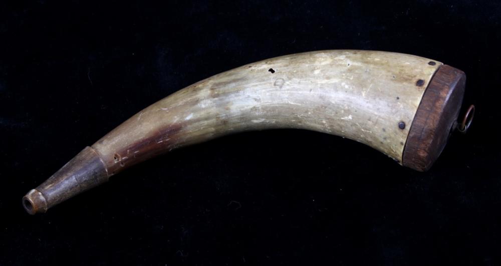 Horn-shaped black powder flask with a dark metal cap and wood band at one end, shown against a dark background.