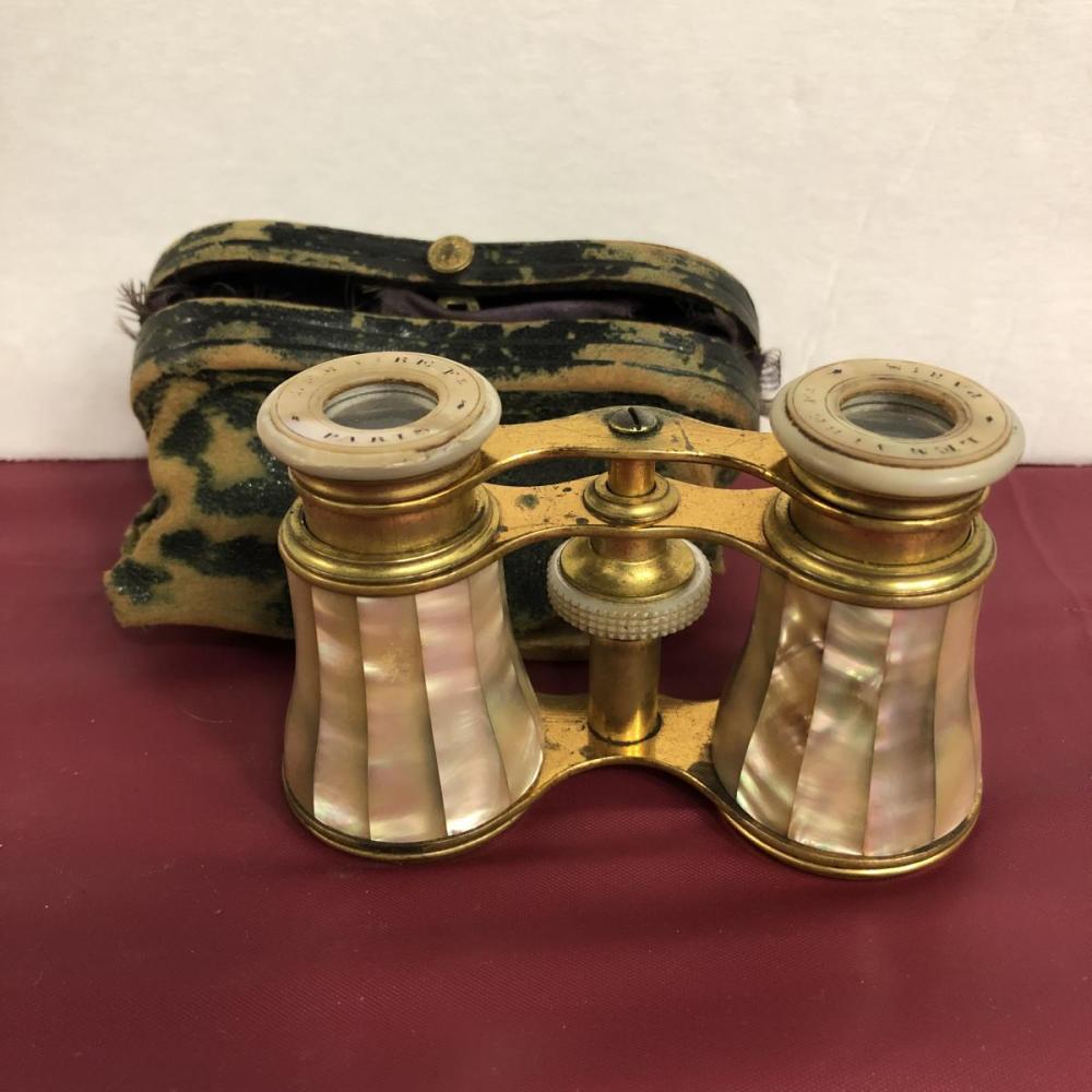 Brass opera glasses with mother-of-pearl style panels and two circular focus lenses in front of a leather case.