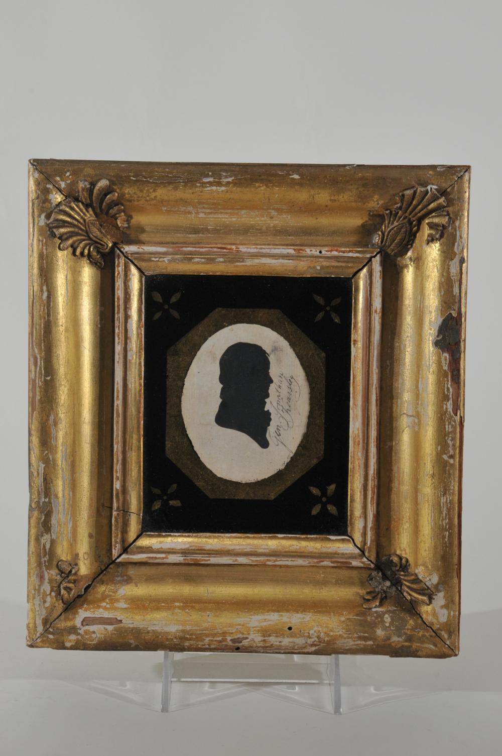 Framed oval silhouette portrait of a man in black profile against a light circular background, surrounded by a dark central mat and decorative gold frame with e