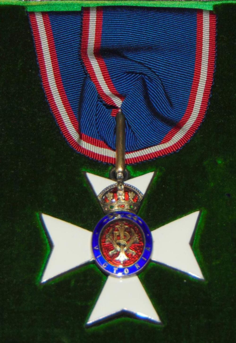 Close-up of a blue-and-red striped ribbon and a white cross medal with a colorful central emblem.