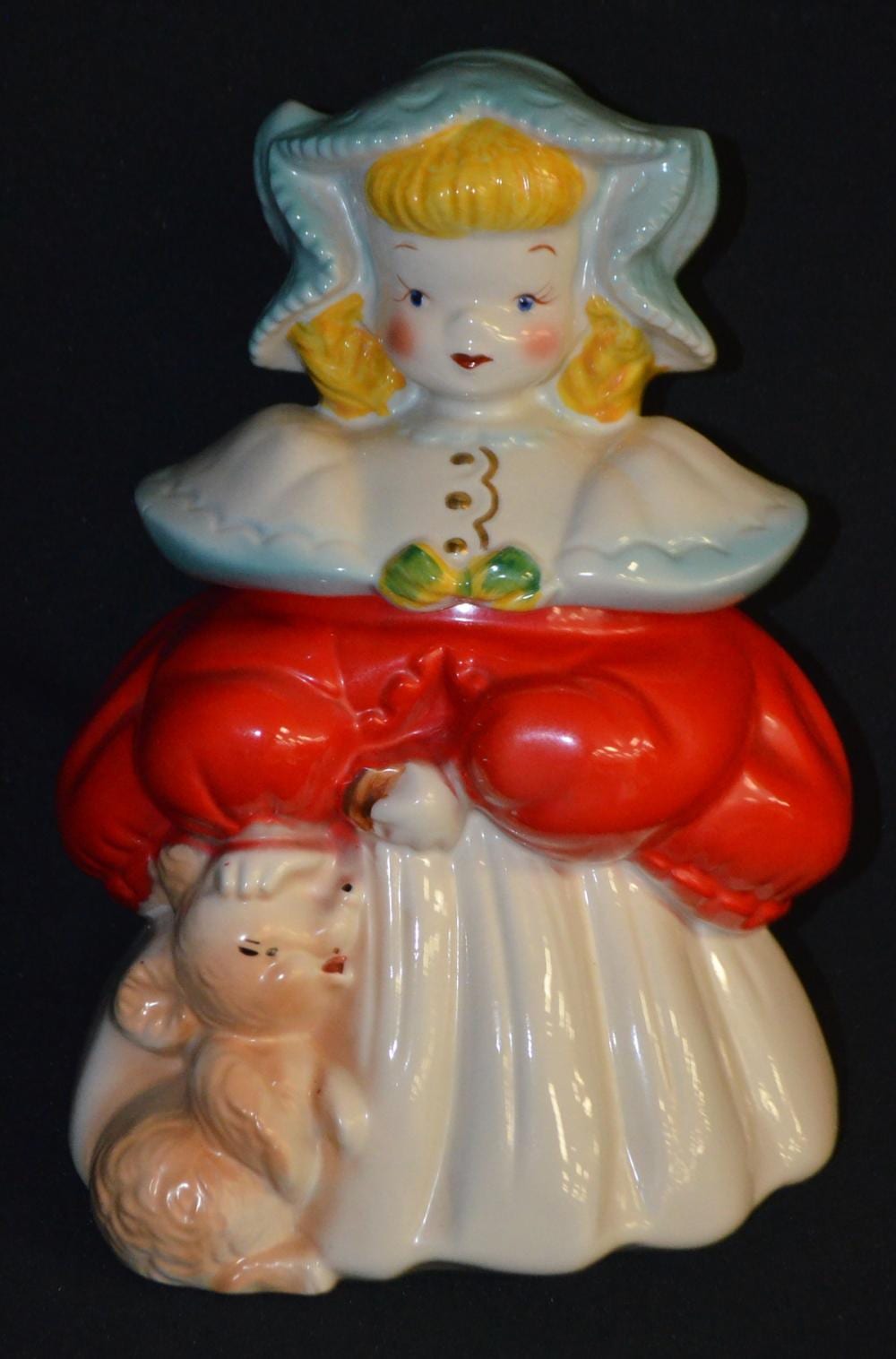 Ceramic cookie jar shaped like a blonde child in a white dress with red collar and bonnet, holding a smaller figure near the bottom.