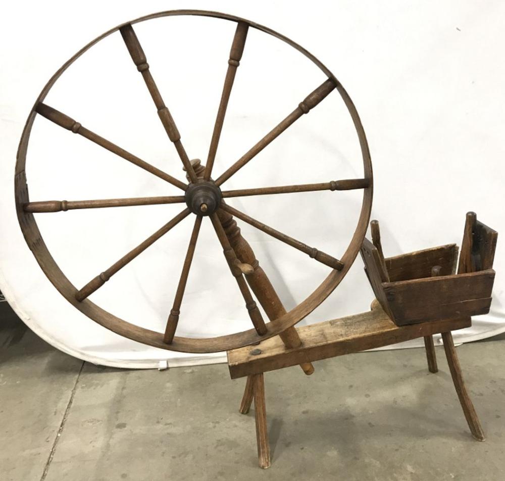 Antique wooden spinning wheel with a large circular wheel, spokes, and a small attached basket or holder.