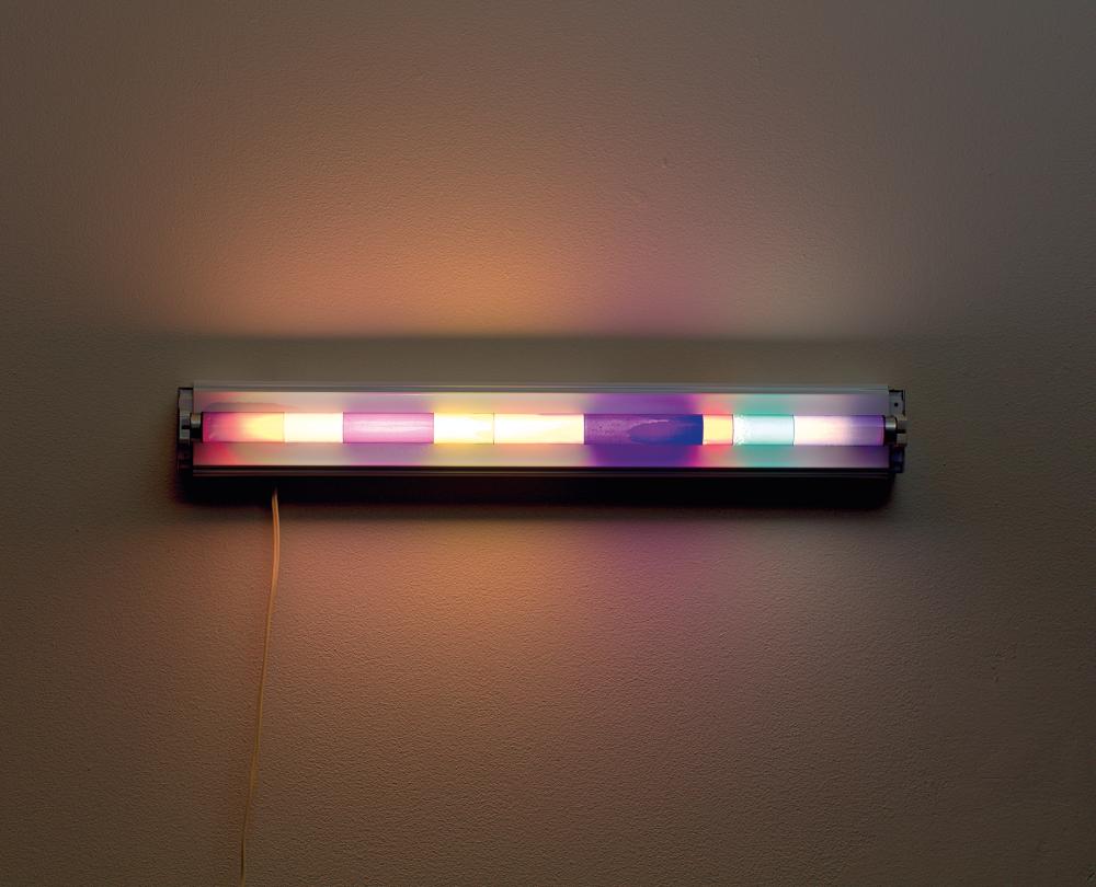 Wall-mounted light fixture with a rectangular bar emitting multicolor glow, including purple, green, and orange tones.