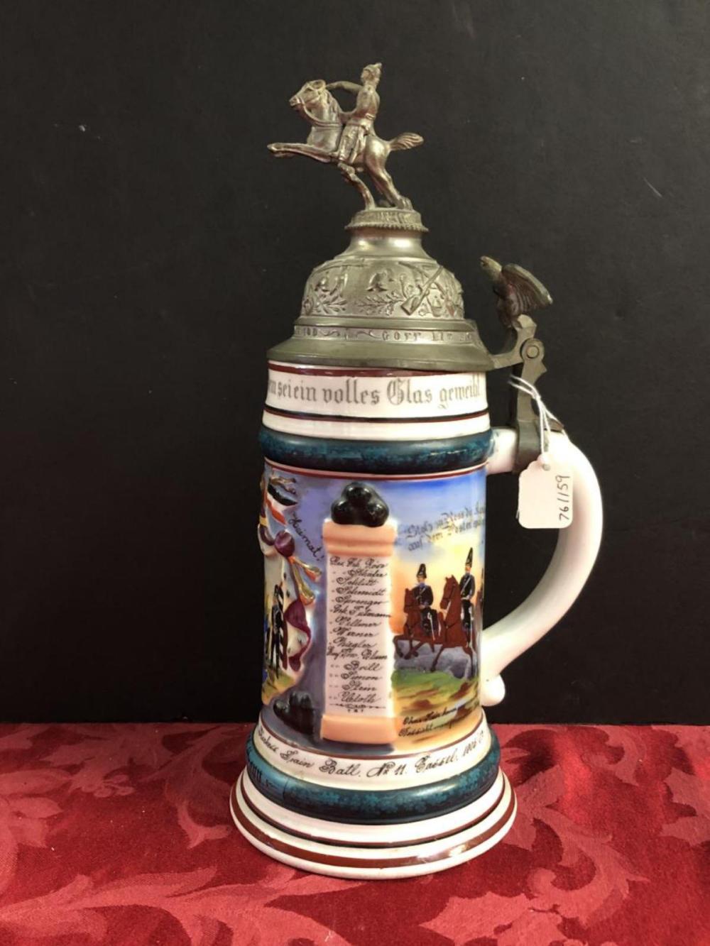 Lidded German beer stein with painted scenes, German-style text band, and a metal figure handle on top.