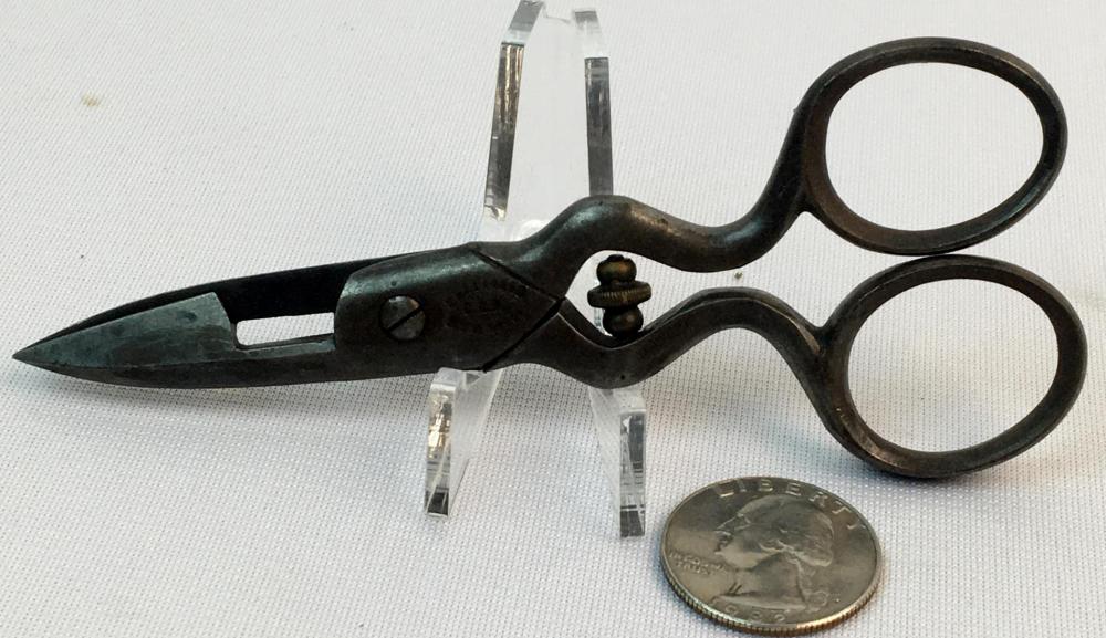 Vintage buttonhole sewing scissors with black handles and two finger rings, laid next to a coin for scale.